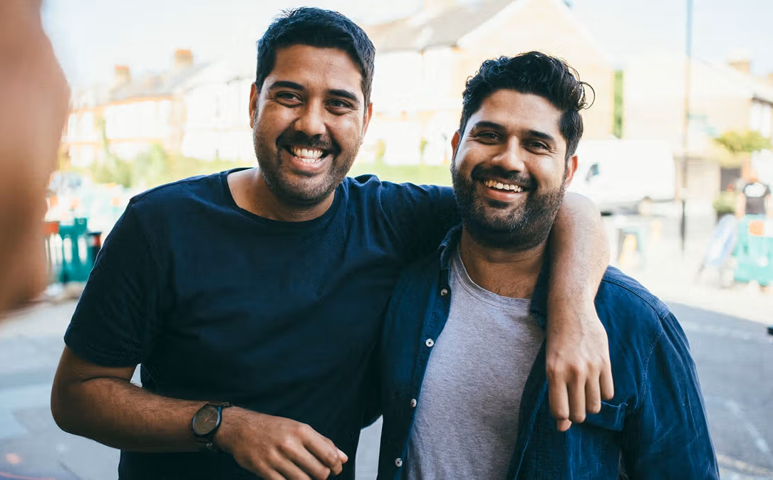 Two smiling men pose together outdoors