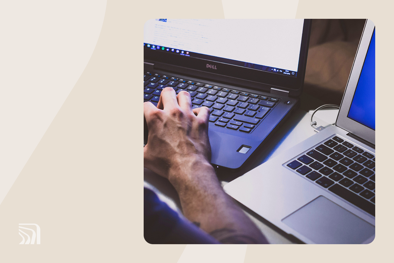 Personne tapant sur un ordinateur portable Dell à côté d’un MacBook, tous deux sur un bureau, dans un environnement à l’éclairage tamisé.