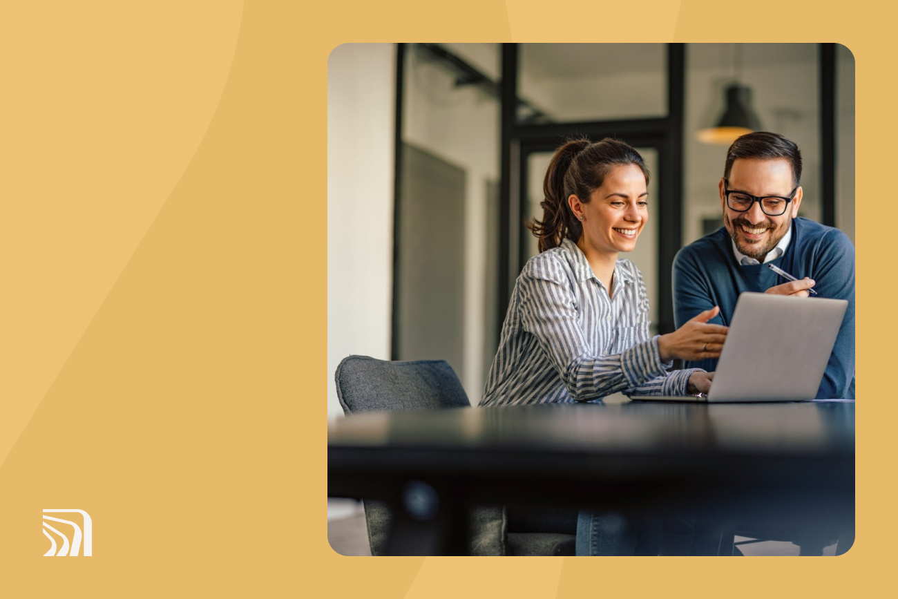 couple sitting at desk looking at laptop with yellow background