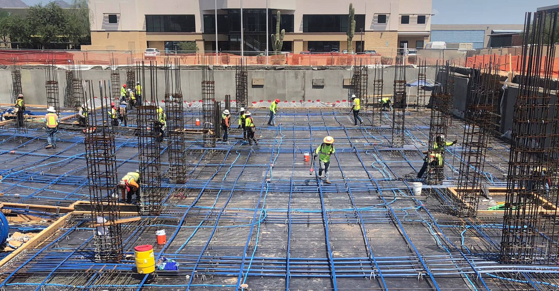 Construction workers wearing safety vests and helmets working on a reinforced concrete structure with blue cables and steel frameworks on a building site.