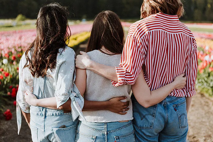 Three people stand with arms around each other, facing a colorful tulip field. They wear casual outfits, creating a sense of unity and friendship.
